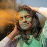 Young woman enjoying Holi festival with vibrant color powder on her face.